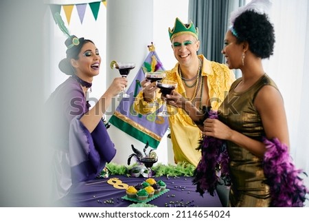 Multiracial group of friends celebrating Mardi Gras and toasting with drinks at home party. 