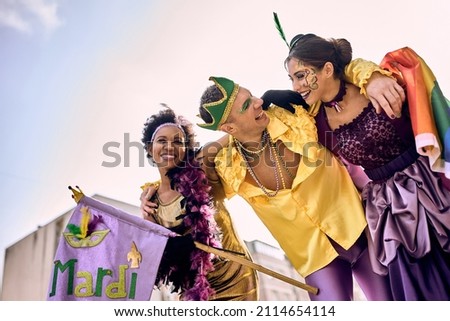 Low angle view of cheerful friends wearing Mardi Gras costumes and make-up and having fun on the street during the carnival.  Royalty-Free Stock Photo #2114654114