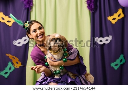 Young woman in Mardi Gras costume having fun with her dog on a party and looking at camera. 