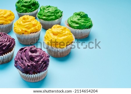 Mardi Gras cupcakes in traditional festival colors on blue background. Copy space. 