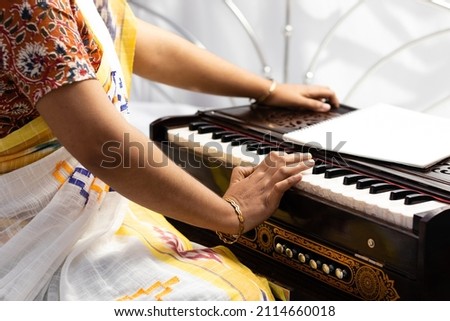 An Indian woman in saree playing harmonium on white background with selective focus Royalty-Free Stock Photo #2114660018