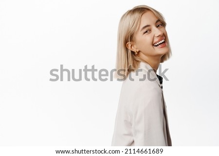 Close up of confident young professional business woman, turn head at camera, standing in profile, smiling and laughing, showing her professionalism and confidence