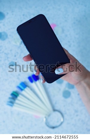 Female arm holding smartphone while sitting at manicure salon.