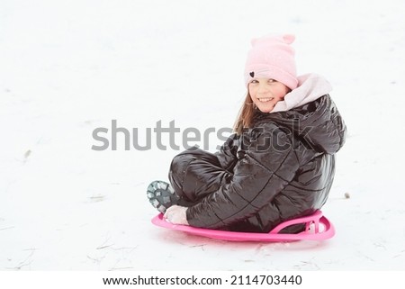Happy little girl sliding down the hill on saucer sled. Girl enjoying slider ride on the snow