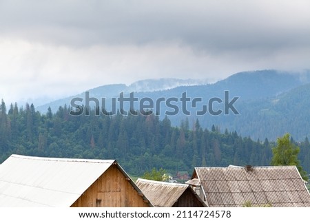 Roofs of village houses on the background of spruce forest and mountains in fog. Ukraine, carpathians.