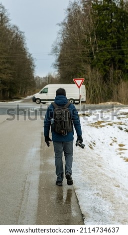A man with a camera and a backpack goes to the car. Winter. view from back