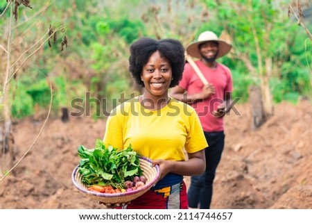 portrait of a beautiful female african farmer carrying basket of vegetable Royalty-Free Stock Photo #2114744657