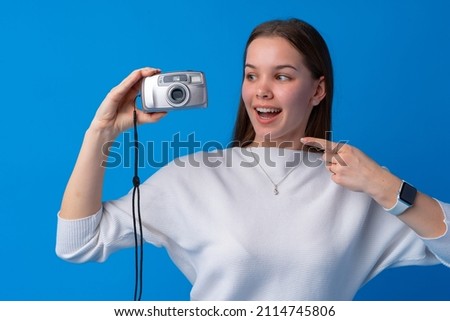 Young caucasian woman holding vintage camera on blue background in studio