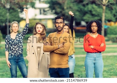 a man with African-American features looks defiantly at the camera, in front of four women. Royalty-Free Stock Photo #2114786939