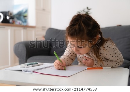 Portrait of cute preschooler child girl drawing with pencils at home while sitting in front of the camera with attentive face. Stock photo