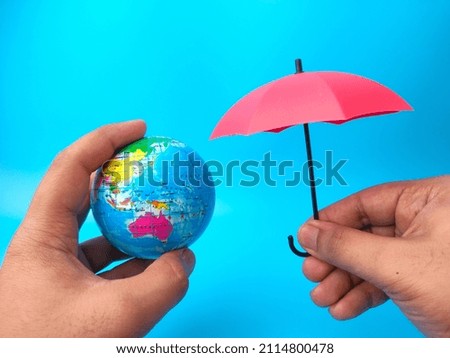 Hand holding earth globe and umbrella on blue background.