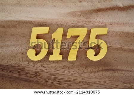 Wooden Arabic numerals 5175 painted in gold on a dark brown and white patterned plank background.