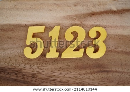 Wooden Arabic numerals 5123 painted in gold on a dark brown and white patterned plank background.