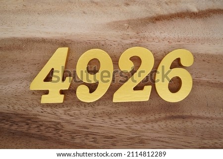 Wooden Arabic numerals 4926 painted in gold on a dark brown and white patterned plank background.