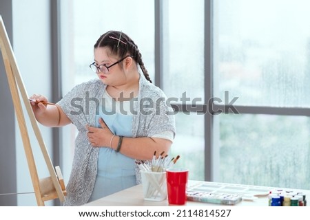 Girl with down syndrome sits next to her mother and is engaged in creativity, drawing a picture.