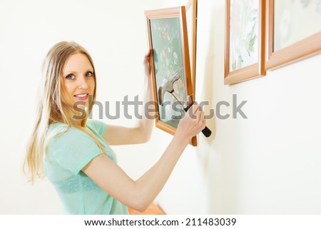 Positive blonde woman hanging  picture with flowers on wall at home