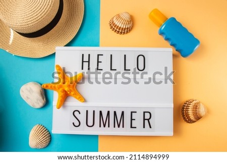 Hello Summer - text on display lightbox on blue and peach bright background, straw hat with seashells.