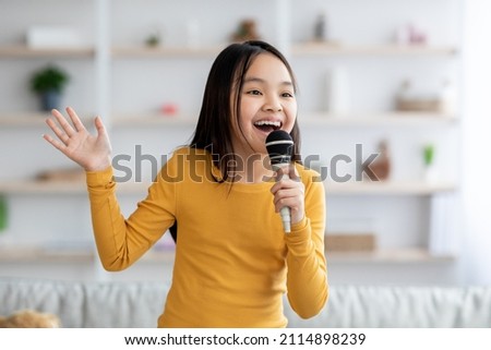 Portrait of cute pretty long-haired korean girl teenager singing at home, using microphone and gesturing, looking at copy space. Child singing karaoke, domestic entertainment for kids concept Royalty-Free Stock Photo #2114898239