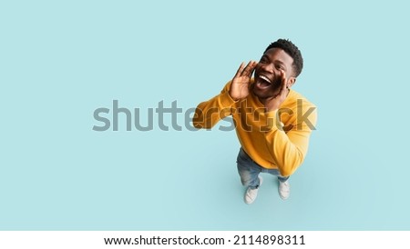 Cheerful african american guy posing over blue studio background, holding hands to mouth and saying something out loud, panorama with copy space. Handsome young black man making announcement, top view Royalty-Free Stock Photo #2114898311