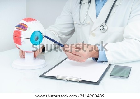 OPHTHALMOLOGIST TEACHING IN THE OFFICE WITH A HUMAN EYE ANATOMY MODEL. FOCUS SELECTED. Royalty-Free Stock Photo #2114900489