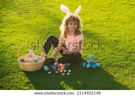 Child boy in rabbit costume with bunny ears hunting easter eggs on grass in spring park. Cute little boy, easter bunny children spring outdoor.