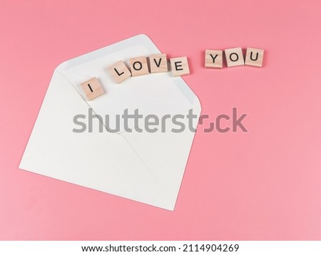 Top view or flat lay of wooden letter "I love you" out of the envelope on pink background.