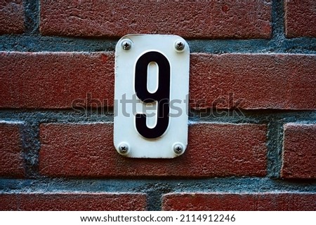 Close Up House Number 9 At Amsterdam The Netherlands. House number 9 on red brick wall with number nine on white metal plate enameled