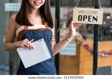 Happy young business owner standing with holding open sign board.