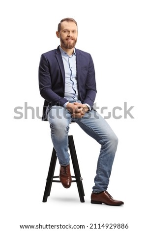 Full length portrait of a man in a suit and jeans sitting on a bar chair isolated on white background Royalty-Free Stock Photo #2114929886