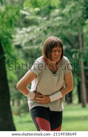 Female jogger with painful face grimace after feeling pain in lower abdomen during running in park Royalty-Free Stock Photo #2114938649