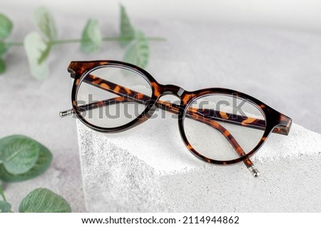 Stylish glasses on a podium made of natural stone. Leopard-colored glasses and plants on a concrete background
