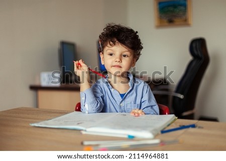 A preschooler learns online at the computer and writes an assignment in a notebook at home. Home online learning