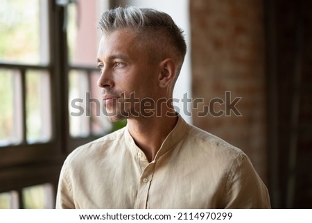 Serious thoughtful handsome millennial grey haired business man, entrepreneur looking at window away in deep thoughts, thinking of business project vision, career, company future. Head shot portrait