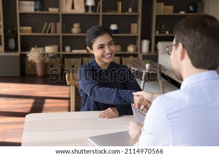Smiling young Indian female job seeker shaking hands with Caucasian hr manager, starting interview meeting or accepting offer proposal, making good first impression talking in modern office room. Royalty-Free Stock Photo #2114970566