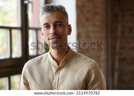 Happy positive millennial business man in casual, company owner, startup leader, professional posing, looking at camera, smiling. Businessman indoor head shot portrait in loft interior