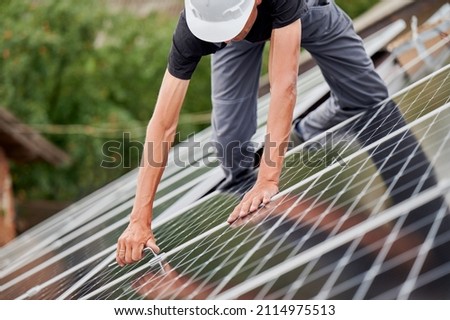 Man technician mounting photovoltaic solar moduls on roof of house. Cropped view of builder in helmet installing solar panel system with help of hex key. Concept of alternative, renewable energy. Royalty-Free Stock Photo #2114975513