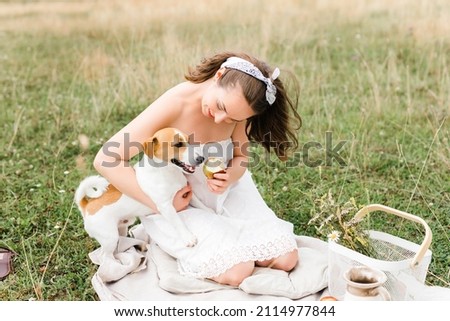 Caucasian beautiful girl on a summer day at a picnic. girl in a white dress and kerchief in a field. jack russell terrier dog playing with the owner. girl and dog playing. man and animal together.
