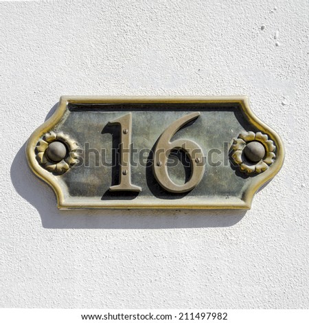 cast bronze house number sixteen on a white stucco wall