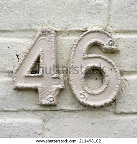 Ceramic house number forty six. White lettering on a white wall