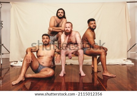 Shirtless and confident. Four body positive men looking at the camera while wearing underwear in a studio. Group of self-assured men embracing their natural bodies together. Royalty-Free Stock Photo #2115012356