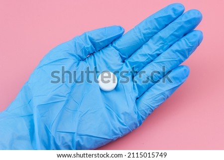 A white pill lies on the palm of your hand in a medical glove on a pink background. Health support.