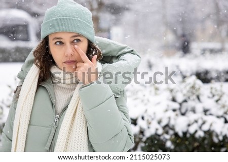 Young woman having itching eyes health problem. Sick woman in winter snow touching her sensitive eye Royalty-Free Stock Photo #2115025073
