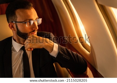 Handsome businessman wearing elegant suit  flying on exclusive private jet - Successful entrepreneur sitting in exclusive business class on airplane, concepts about business and trasportation Royalty-Free Stock Photo #2115028205