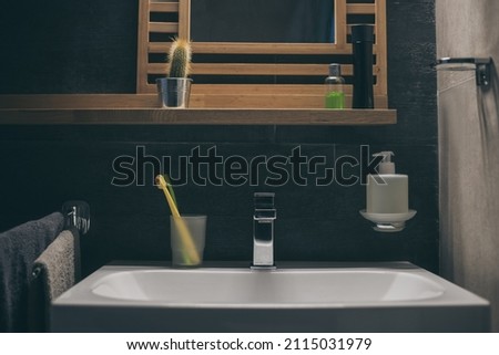 Closeup view of a sink with towels, toothbrush and soap dispenser. Modern environment bathroom fixtures with steel faucet. Cleanliness, health, recycling, pollution, cleaning, ethics, hygiene concept