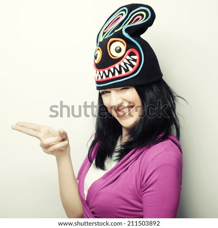 Playful young woman in funny hat with rabbit, studio shot