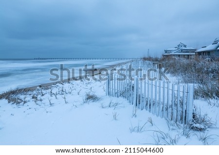 Rarely occurring snow blankets the beach dunes in winter along the Atlantic Ocean in Duck, North Carolina on the Outer Banks. Royalty-Free Stock Photo #2115044600
