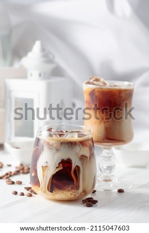 Iced coffee with cream and natural ice on a white wooden table.