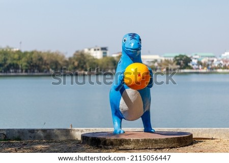Blue dinosaur statue holding a yellow ball standing by the lake