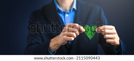 Businessman holding a green heart leaf. Company corporate social responsibility and environmental concern. Environmental and Ecology Care Concept.  Royalty-Free Stock Photo #2115090443