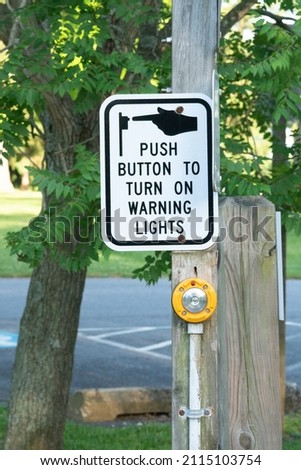 metal traffic sign push button to activate pedestrian crossing intersection warning lights on a pole across the street is solar powered and people activated